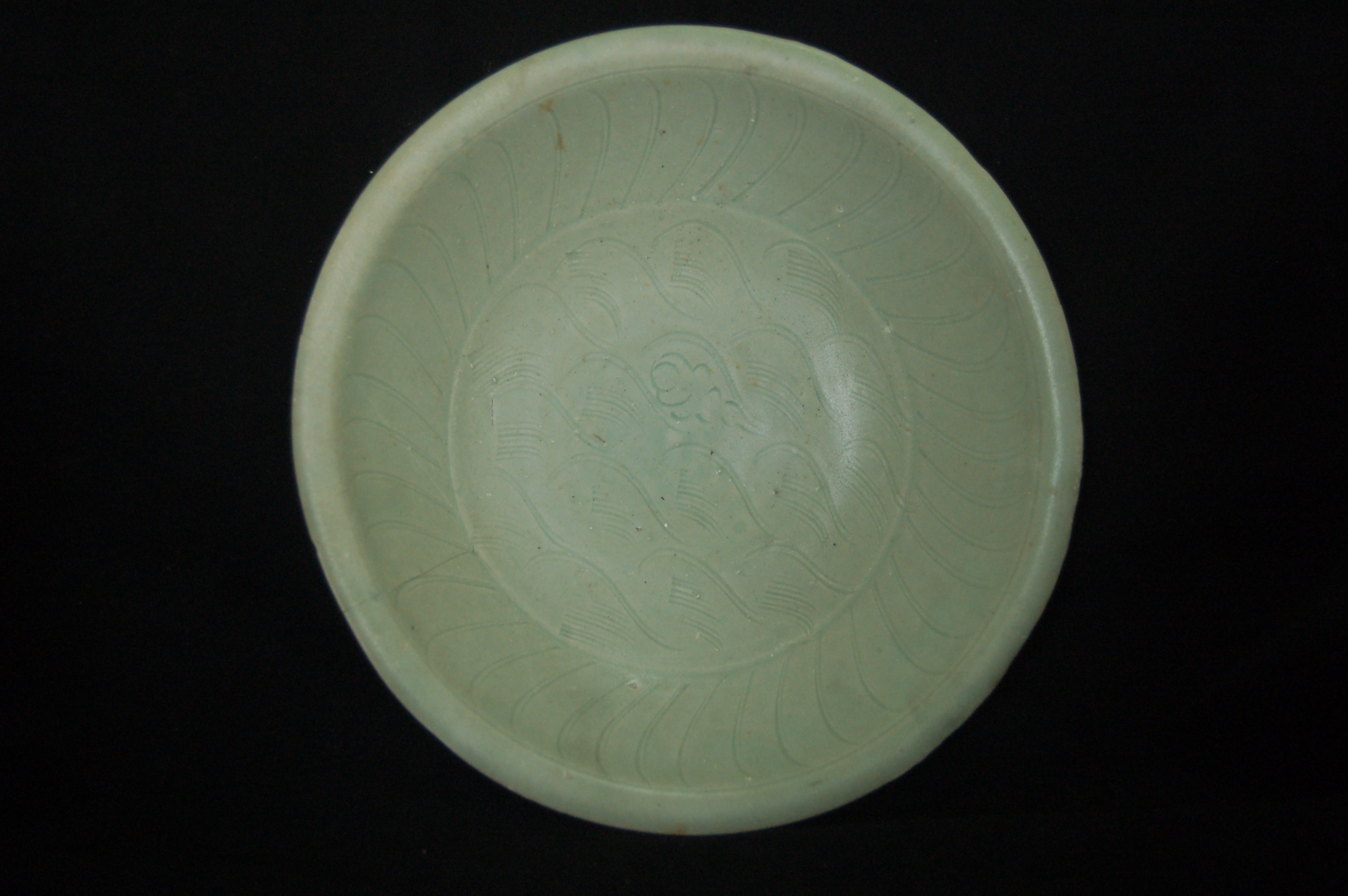Green-glazed shallow bowl with an everted rim, rounded walls and a carved foot-ring. The well is decorated with incised waves and a central cloud while the cavetto displays paired striations. Diameter 22 cm, height 6 cm.