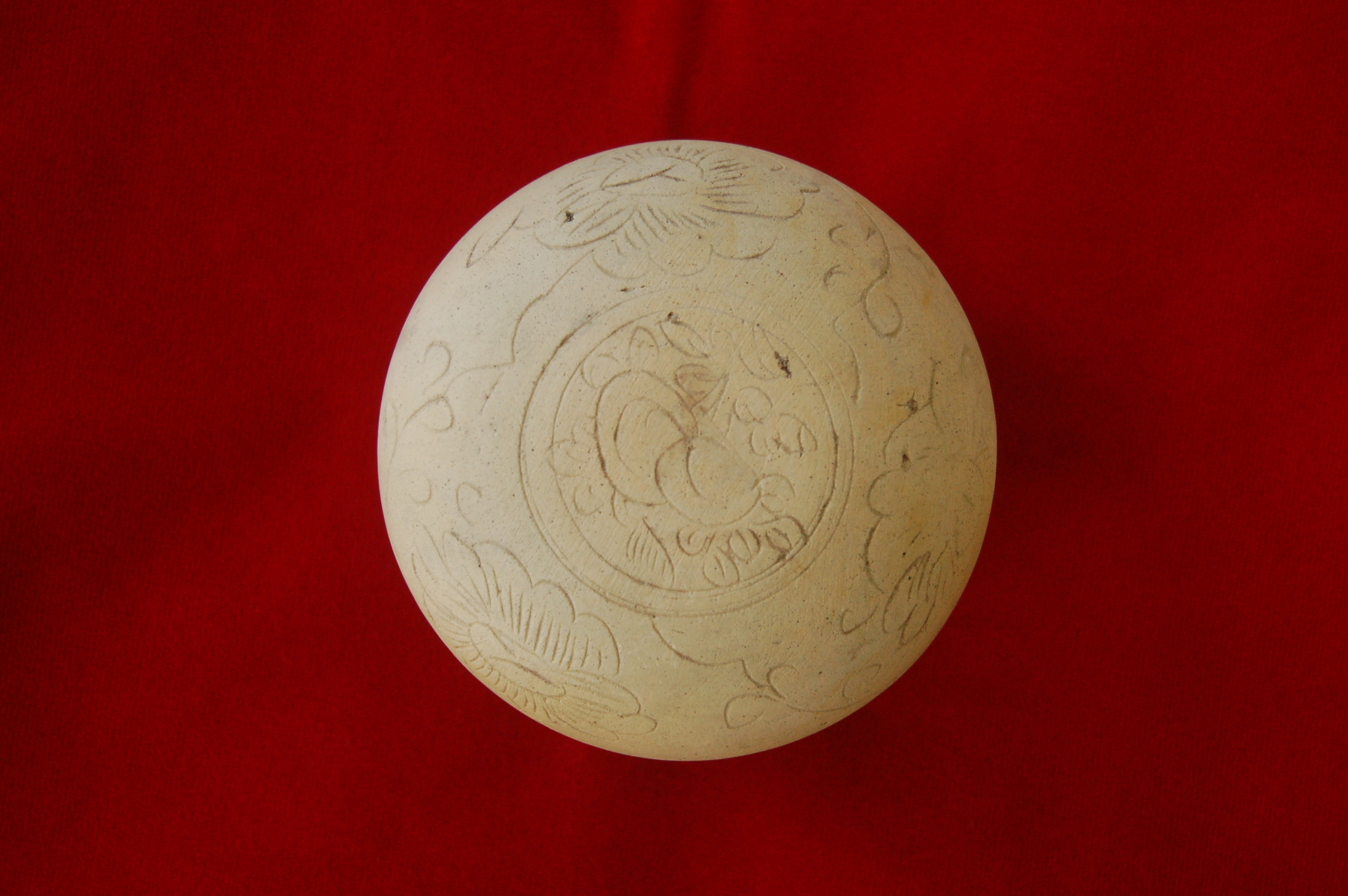 Covered box with an incised floral decoration on the cover, featuring a pair of peaches in the centre. Perfectly round with a carved foot-ring. Diameter 8.5 cm, height 5 cm.