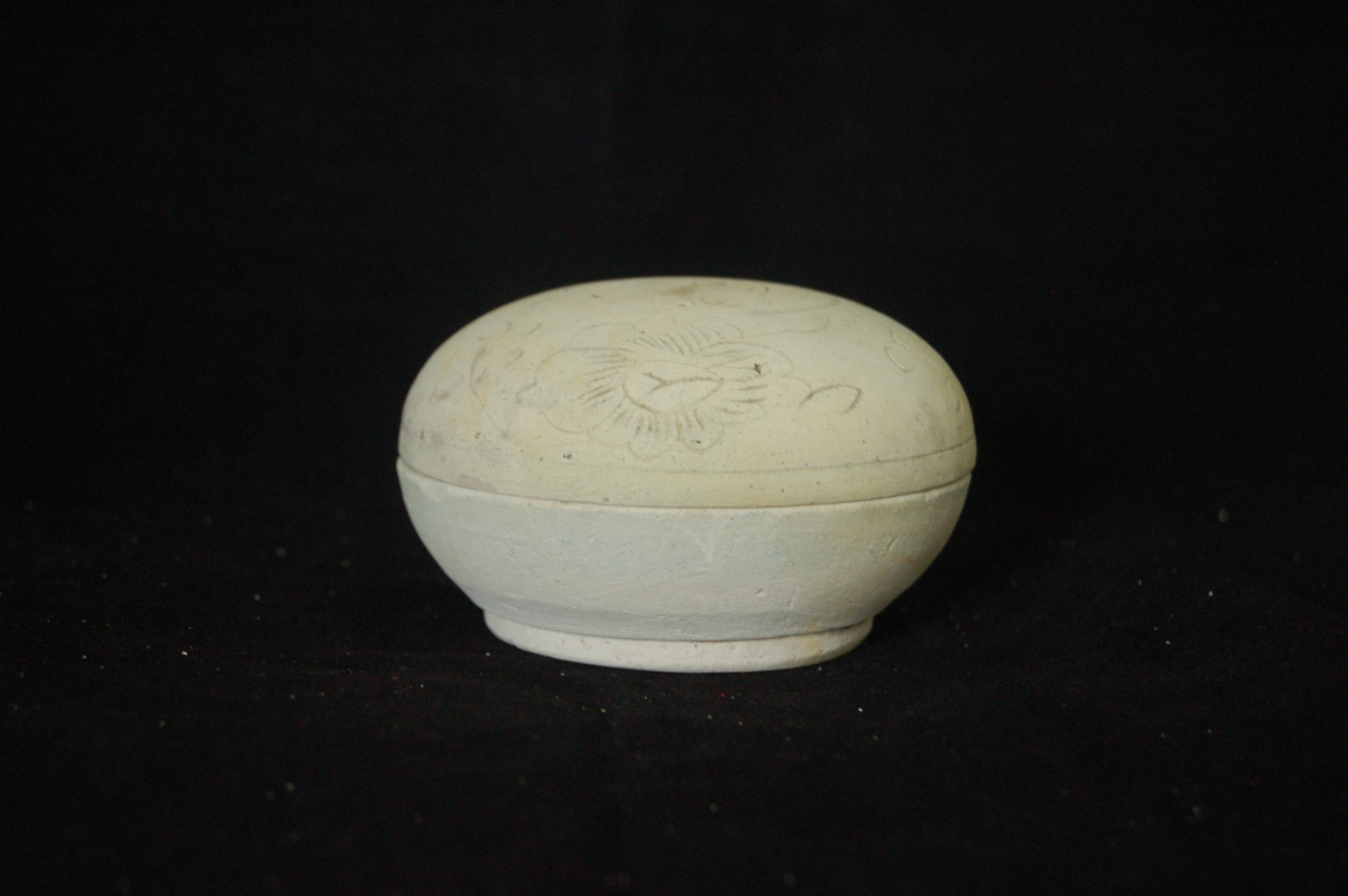Covered box with an incised floral decoration on the cover, featuring a pair of peaches in the centre. Perfectly round with a carved foot-ring. Diameter 8.5 cm, height 5 cm.