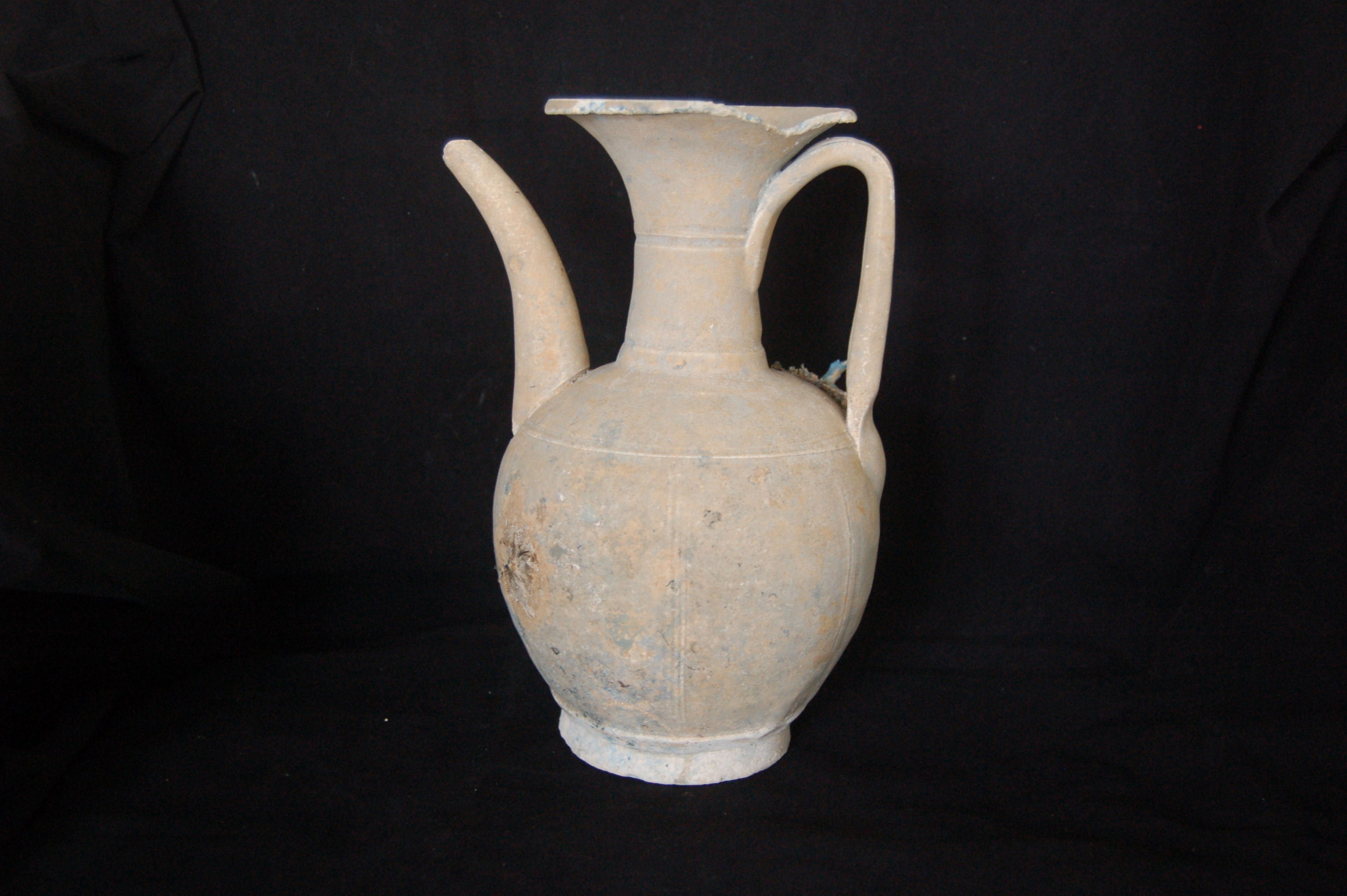 Ewer with a long neck, flared mouth, a strap handle and curved spout.  The carved foot-ring is slightly flared. Decorated with incised rings around the neck and shoulder, and vertical triplets around the body. Diameter 14 cm, height 23.5 cm.