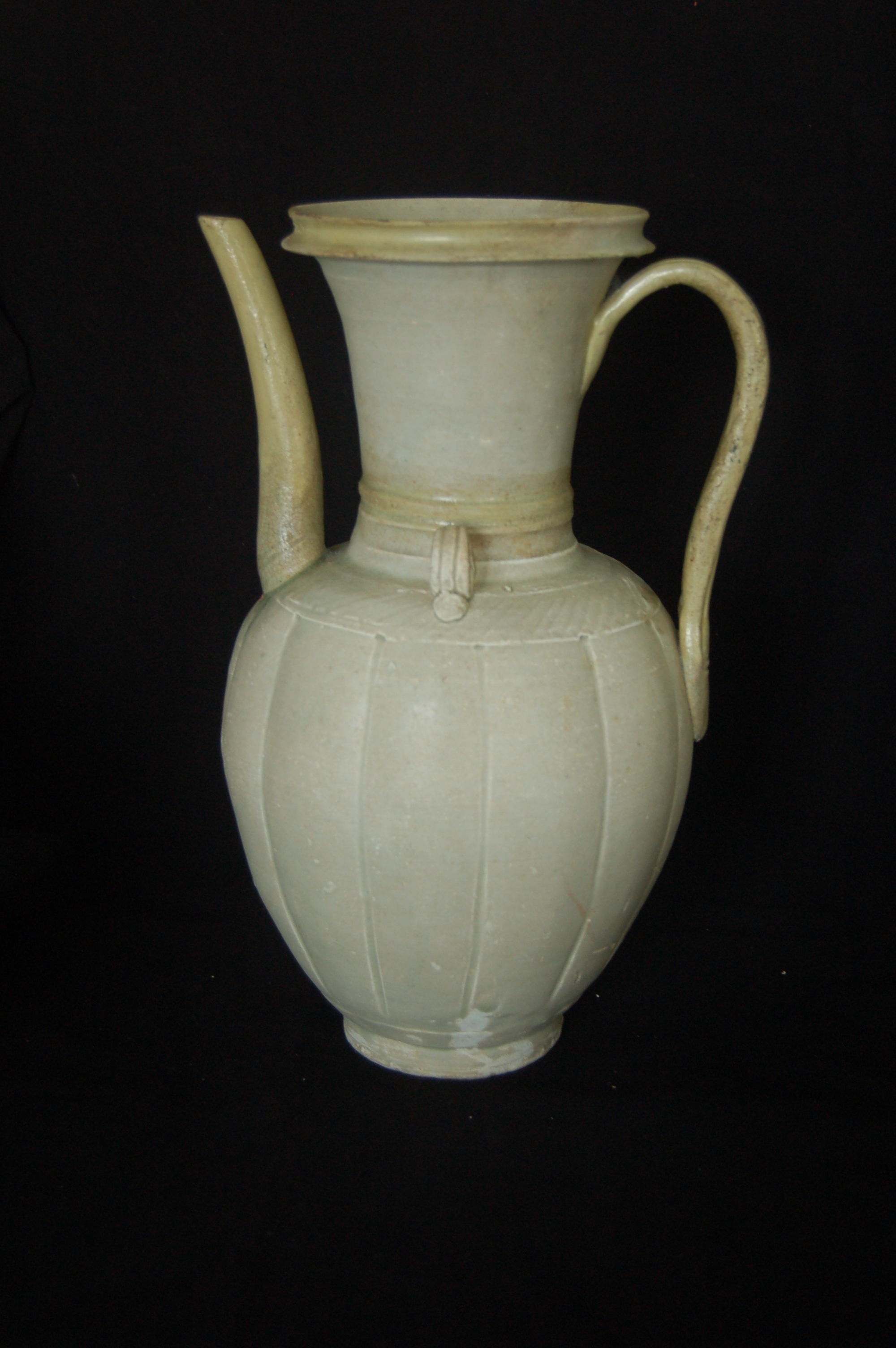Large ewer with a long neck, flared mouth, flanged mouth-rim, a strap handle, and curved spout. The carved foot-ring is straight. The body is slightly lobed with each lobe divided by vertically incised lines. The lower neck is decorated with flanges and the shoulder has spiral striations. Diameter 18 cm, height 33 cm. Note: the neck, spout and handle have been repaired.