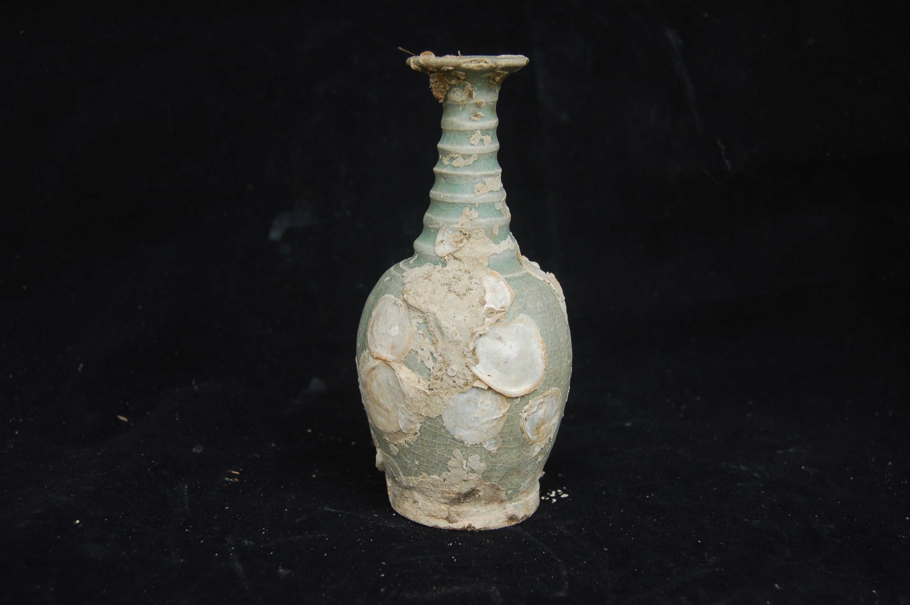 Vase with a green glaze and subtly lobed body. The rings around the tall tapering neck are carved so deeply that they form flanges. The mouth is elegantly flared, while the carved foot-ring is near vertical. Diameter 6.5 cm, height 13.5 cm.