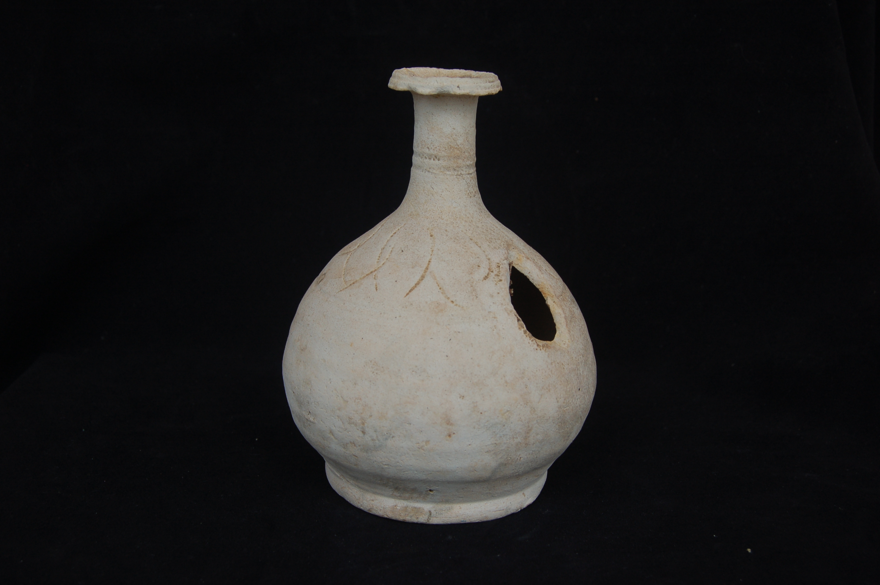 Kendi with globular body decorated with incised lotus leaves around the shoulder. Long straight neck with flattened mouth-rim, and a flat base. Spout missing. Diameter 12 cm, height 17 cm.