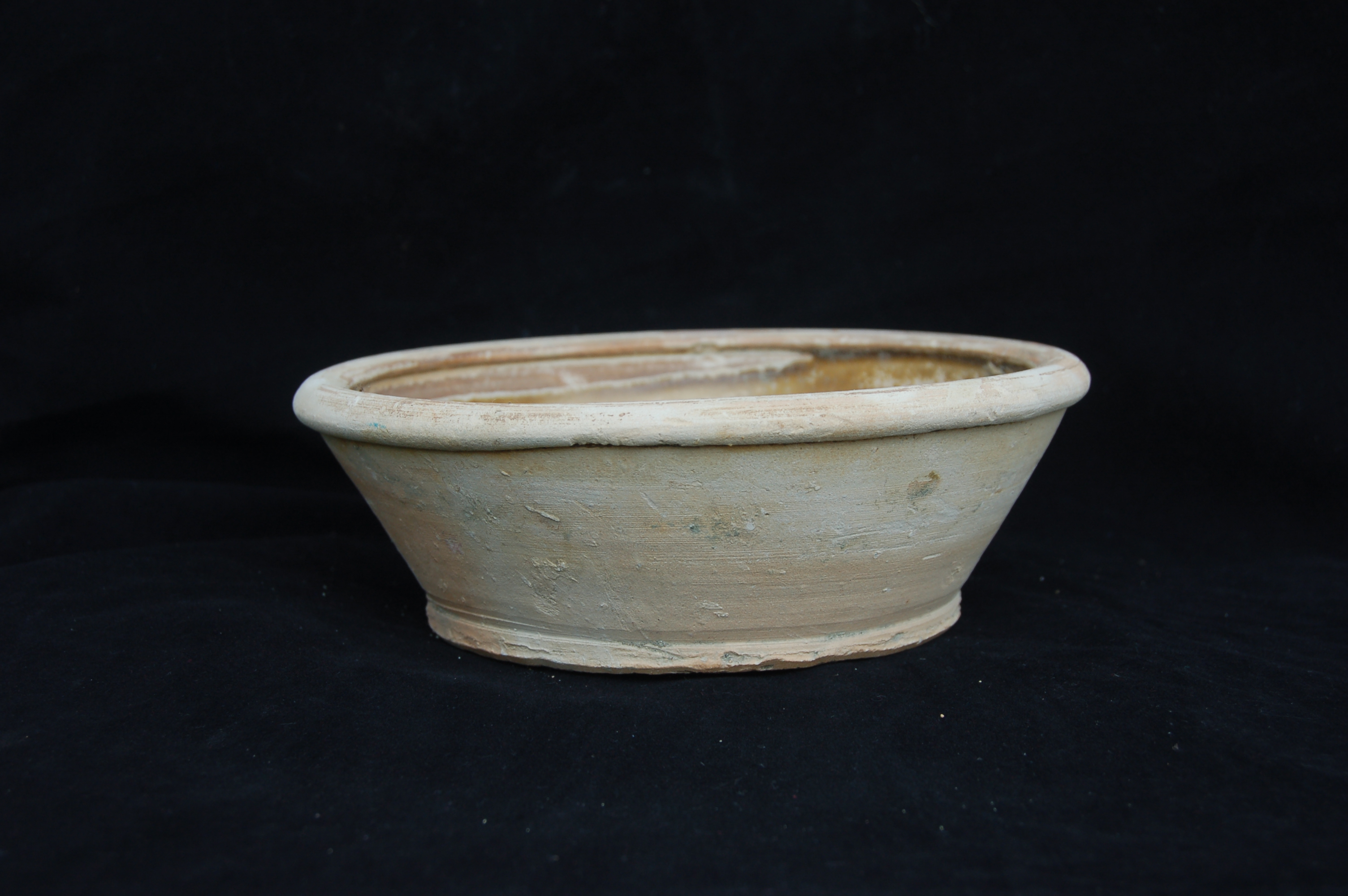Small basin with olive-green glaze, decorated with an impressed floral motif. It has straight walls with a folded rim, and a flat base. Diameter 20 cm, height 7 cm.