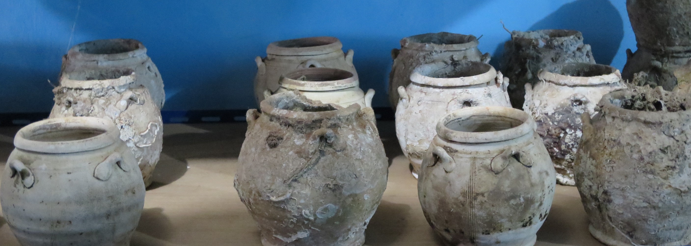 Medium wide-mouth jars with four lug-handles, a folded mouth-rim and a flat base. Some are decorated with triplets of vertical incised lines.